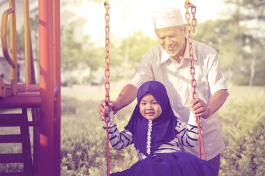 Yaşlı adam sallanırken torununu tutuyor.