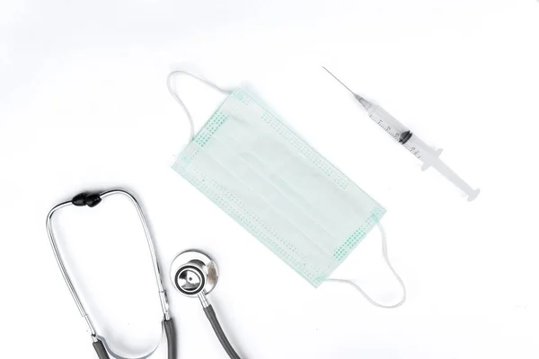 Stethoscope and syringe around face mask in white — Stock Photo, Image