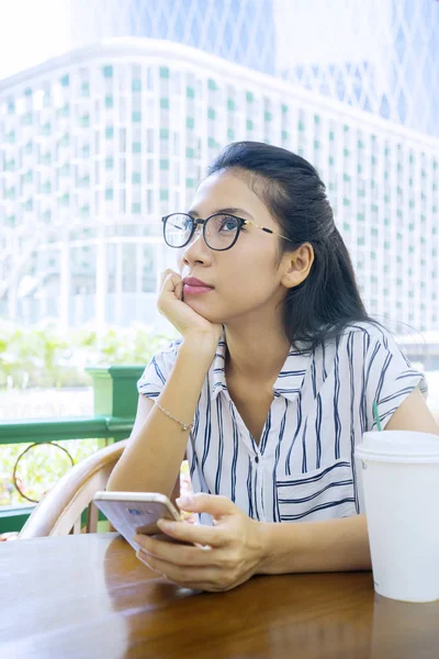 Mujer sostiene el teléfono móvil y sentarse en la cafetería — Foto de Stock