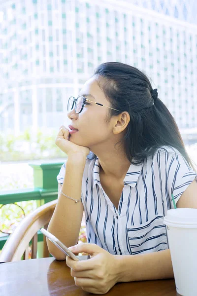 Woman sitting in cafe while holding mobile phone — Stock Photo, Image