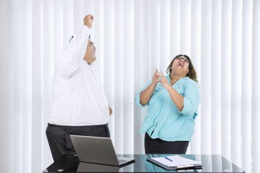 Portrait of fat Asian couple wearing formal attire while dancing & laughing in their office
