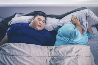 Şişman Asyalı bir kadının yatak odasındaki yatakta uyurken kocasının horlamasından rahatsız olmasının en iyi portresi.