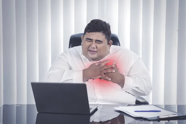 在办公室的笔记本电脑前 一个肥胖的亚洲男人痛苦地捂住胸膛的画像 — 图库照片