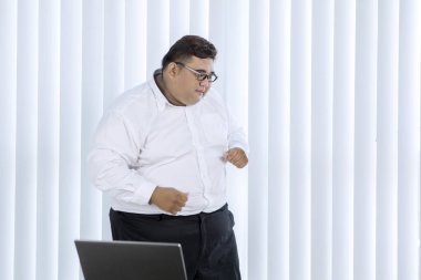 Portrait of fat Asian businessman wearing formal attire while cheering & dancing for his finished job in his office