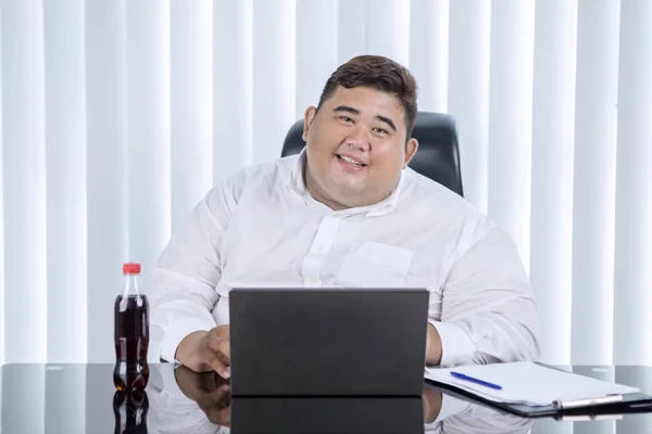 彼のオフィスのノートパソコンで働いている間 カメラで笑顔の太ったアジアのビジネスマンの肖像画 — ストック写真