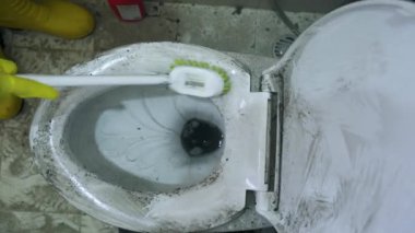 Erkek hademe kirli klozet kapağını fırçalıyor.