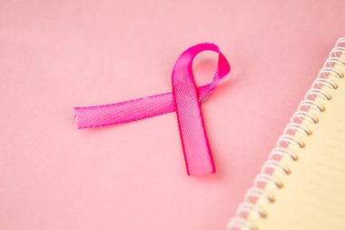 Pembe kurdele, pembe karton arka planda izole edilmiş bir defterin yanında yatıyor.