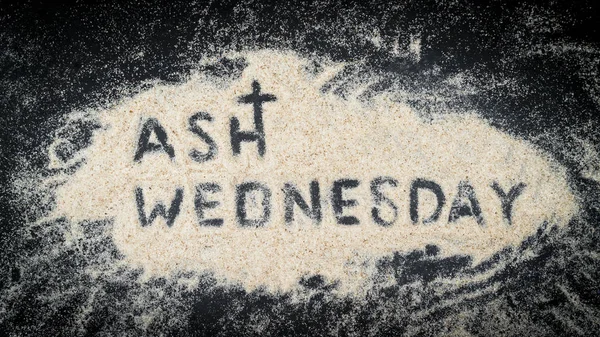Flat lay of ASH WEDNESDAY word written on white sand with black wooden background