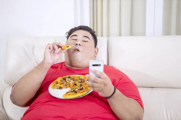 Portrét Tlustého Asiata Pomocí Mobilního Telefonu Zatímco Žvýká Pizzu Svém — Stock fotografie