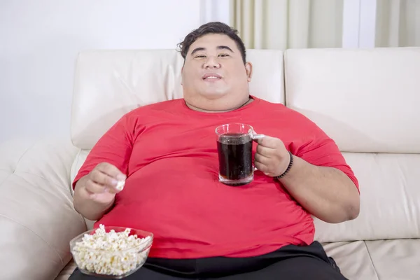 脂肪アジアの男の肖像画テレビのエンターテイメントを見ながら コーラのガラスを保持 彼のリビングルームでいくつかのポップコーンをつかむ — ストック写真