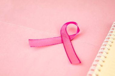 Pembe kurdele, pembe karton arka planda izole edilmiş bir defterin yanında yatıyor.