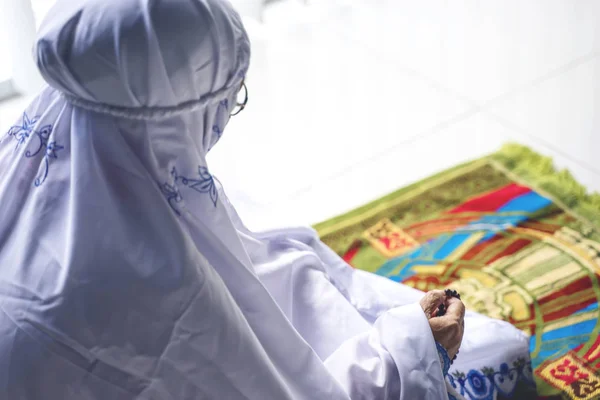 Senior muslim woman praying on praying mat while holding rosary beads