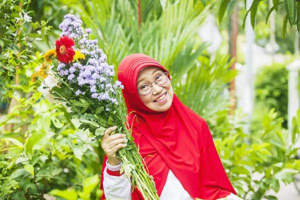 Atraktivní Starší Muslimka Usmívá Kamery Zatímco Drží Květiny Zahradě — Stock fotografie