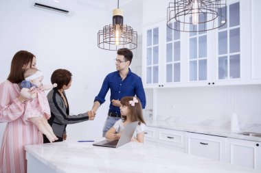 Güzel Asyalı iş kadını portresi beyaz müşterisiyle mutfakta mutlu ailesiyle el sıkışıyor.