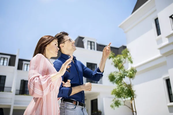 一对成熟的白人夫妇相互拥抱的侧面肖像 一边指着新房子 一边站在院子里 — 图库照片
