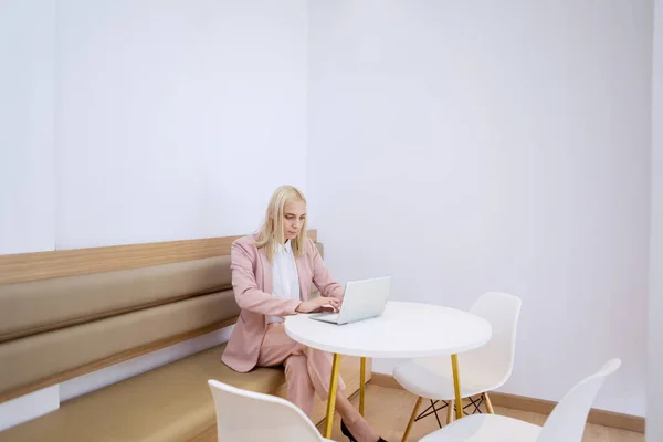 美しいブロンド白人ビジネスマン女性座っています上のベンチで作業しながら彼女のラップトップでザコワーキングスペース — ストック写真