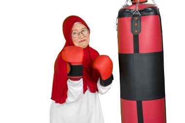 Beyaz arka planda izole edilmiş, kameraya gülümserken boks eldiveni giyen yaşlı Müslüman kadının portresi.