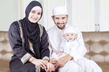 Güzel Müslüman aile evdeki kanepede otururken kameraya gülümsüyor.