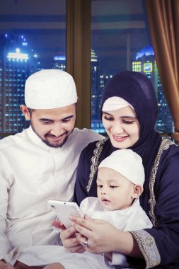 Küçük mutlu Müslüman çocuk ve ailesi gece pencerenin yanında cep telefonu kullanıyor.