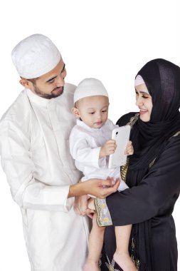 Mutlu küçük Müslüman çocuk ve ailesi stüdyoda beyaz arka planda izole bir şekilde dururken birlikte cep telefonu kullanıyorlar.