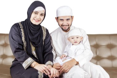 Mutlu Müslüman aile kanepede oturmuş kameraya bakıp gülümsüyor.