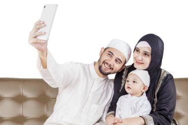 Mutlu Müslüman aile koltukta otururken cep telefonuyla selfie çekiyor.