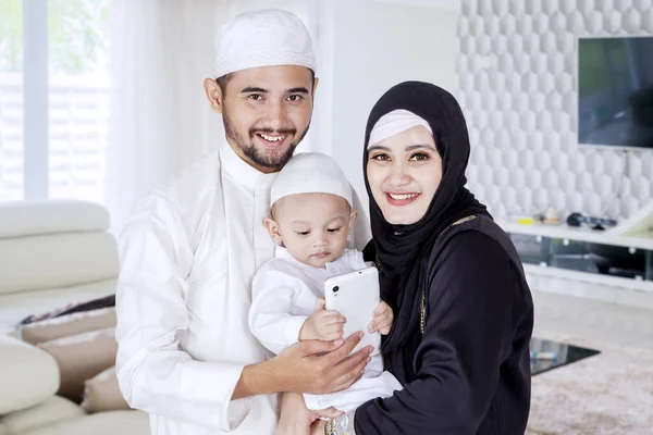 幸せなイスラム教徒の家族と彼らの息子は自宅で携帯電話を使用している間 カメラを見て笑顔 — ストック写真