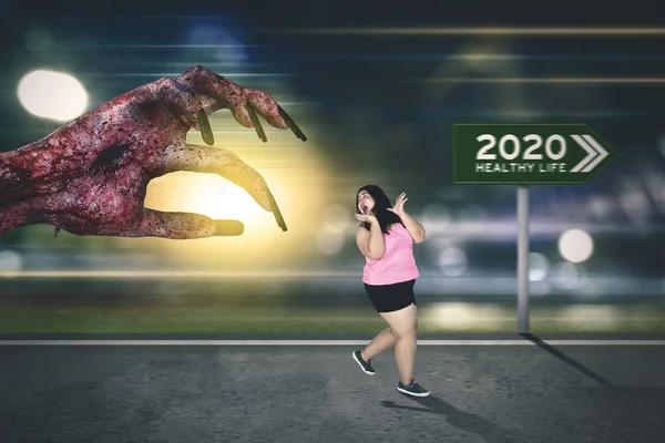 Scared overweight woman escaping from a big scary zombie hand