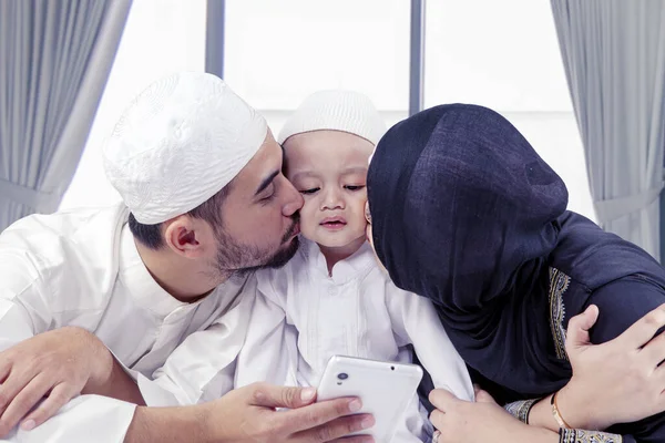 Young Muslim Parents Kissing Son While Using Mobile Phone Bed — Stock Photo, Image