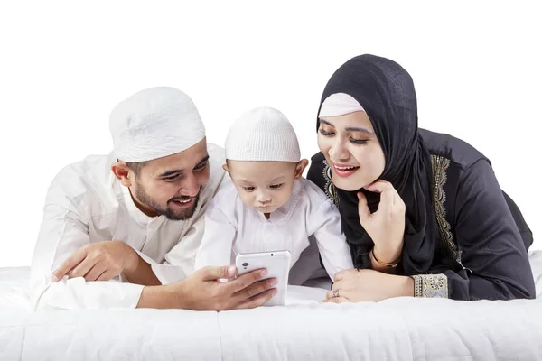 自宅のベッドの上に携帯電話を使用して若いイスラム教徒の両親と彼らの息子の肖像画 — ストック写真