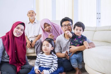 Büyük mutlu Asyalı Müslüman aile oturma odasında dinlenirken neşeyle televizyon izliyor.