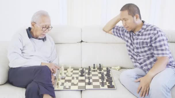 年轻人和他的父亲坐在客厅里下棋的侧视图 — 图库视频影像