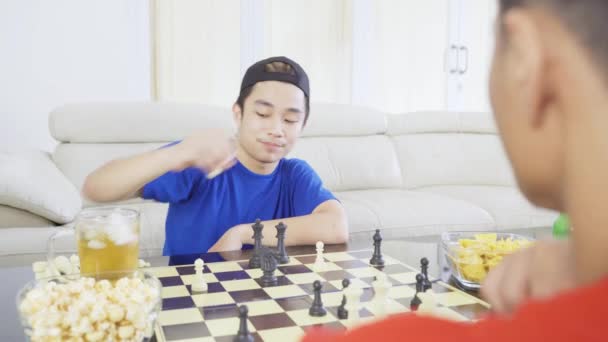 テーブルの上で食べ物や飲み物とリビングルームに座っている間 一緒にチェスをしている2人の若い男性の肖像画 — ストック動画