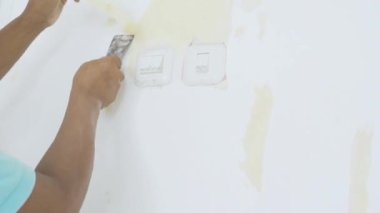  Delikanlının elleri eski duvar kağıtlarını duvardan soyar.