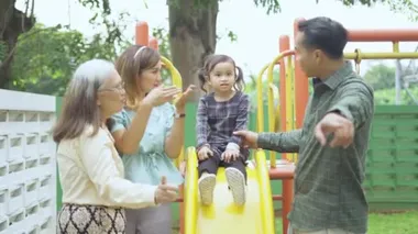 Küçük kız ailesiyle oyun parkında oynuyor.