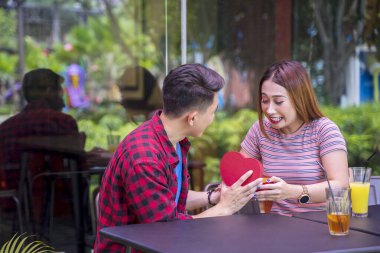 Restoranda otururken kız arkadaşına hediye veren genç adamın portresi. 