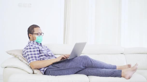 Uomo Indossando Maschera Lavorando Con Computer Portatile Sul Divano — Video Stock