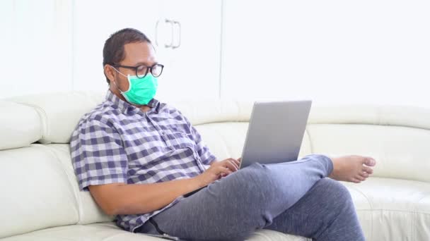 Uomo Indossando Maschera Lavorando Con Computer Portatile Sul Divano — Video Stock