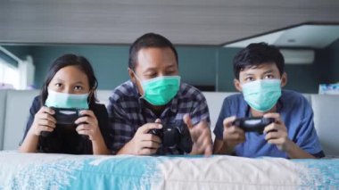 Çocuklar ve babalarının portresi video oyunu oynarken tıbbi maske takıyor ve evde kalıyorlar. 