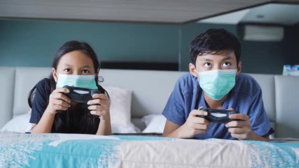 妹妹和弟弟一起玩电子游戏 同时在床上戴医疗面具的肖像 — 图库视频影像