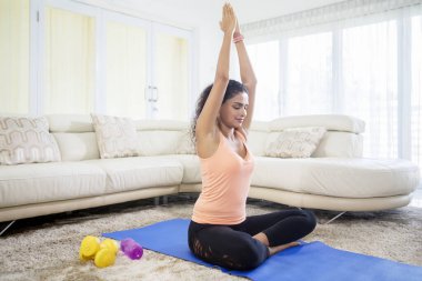 Yatakta yoga yaparken elini kaldıran güzel bir kadın resmi. 