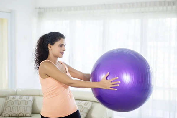 リビングルームでピラティスボールを保持しながら練習を行う魅力的な女性の側面図 — ストック写真