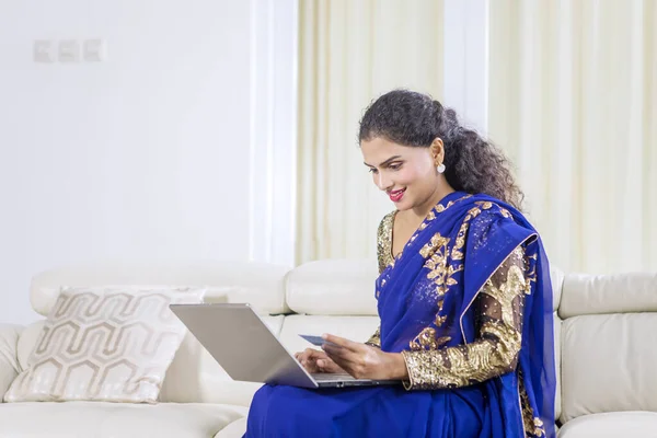 在家里使用笔记本电脑和信用卡时穿着蓝色传统服装的漂亮女人的画像 — 图库照片