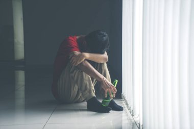 Şişede bira tutarken perdenin yanında oturan depresif adamın portresi.