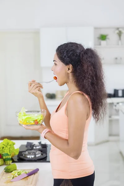 キッチンに立ちながら新鮮な野菜を食べる巻き毛の女性の側面図 — ストック写真