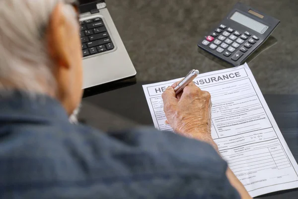 Oudere Man Vullen Ziektekostenverzekering Formulier Met Laptop Rekenmachine Tafel Thuis — Stockfoto