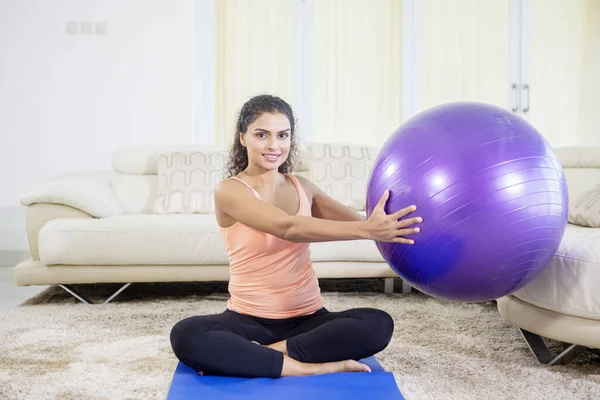 Portrait of indian woman doing yoga exercise while holding pilates ball on the mattress