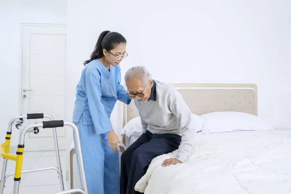 Красивая Медсестра Помогает Старшему Пациенту Сидеть Кровати Стоя Спальне — стоковое фото