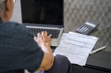 Masada dizüstü bilgisayar ve emeklilik başvuru formu ile çalışan kıdemli bir adam var.