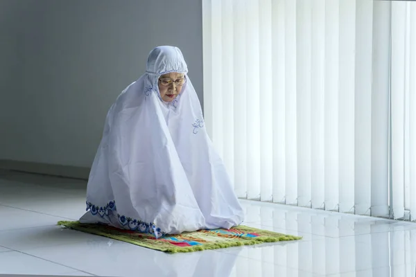 高级穆斯林妇女坐在祈祷席上做礼拜的画像 — 图库照片